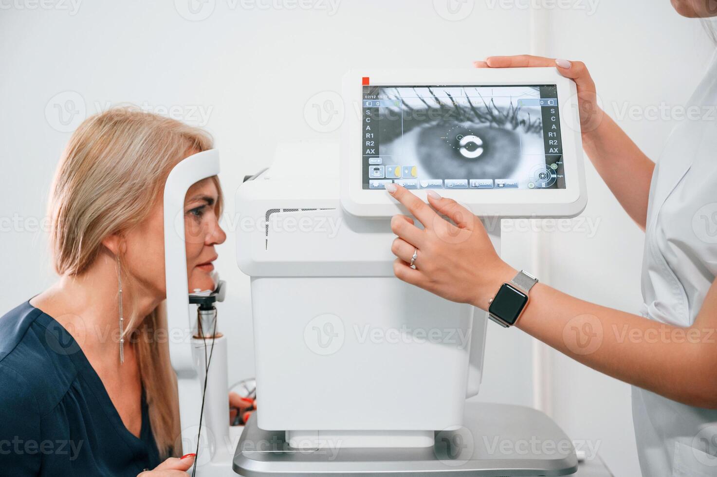 Eye is on the monitor. Woman's vision is tested by clinic worker that using special device photo