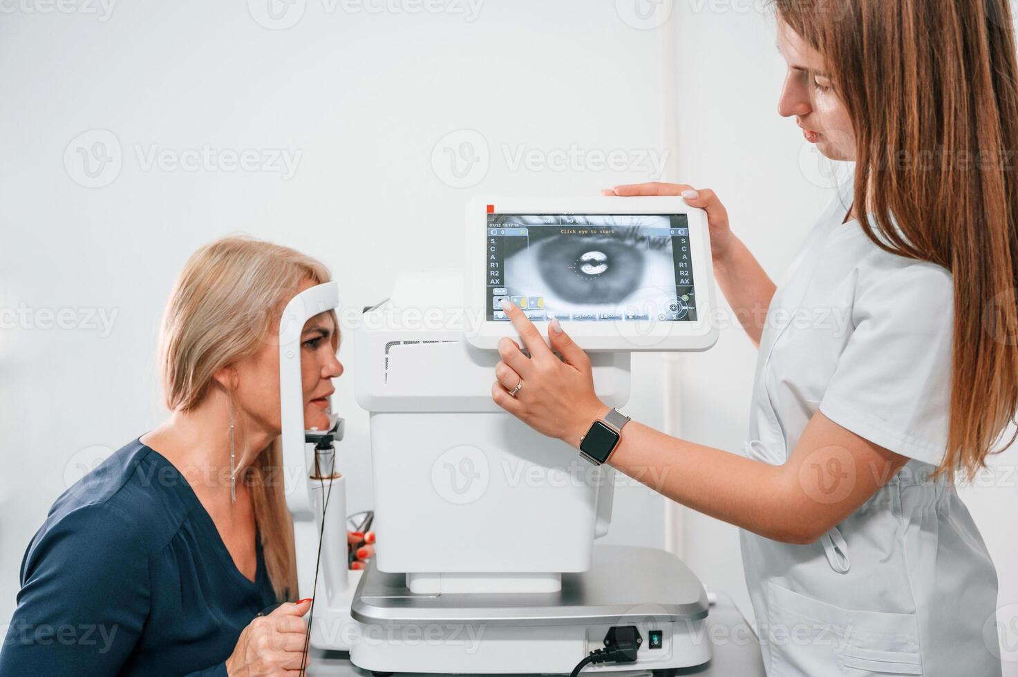 Eye is on the monitor.. Woman's vision is tested by clinic worker that using special device photo