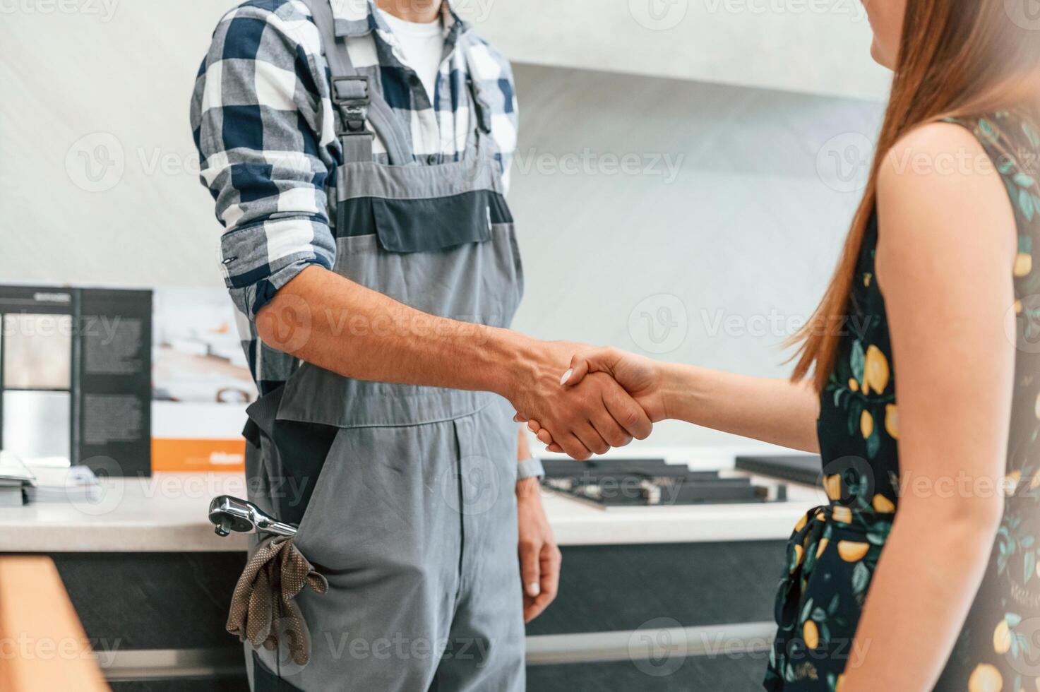 Plumber in uniform helped woman, on the kitchen. Doing handshake photo