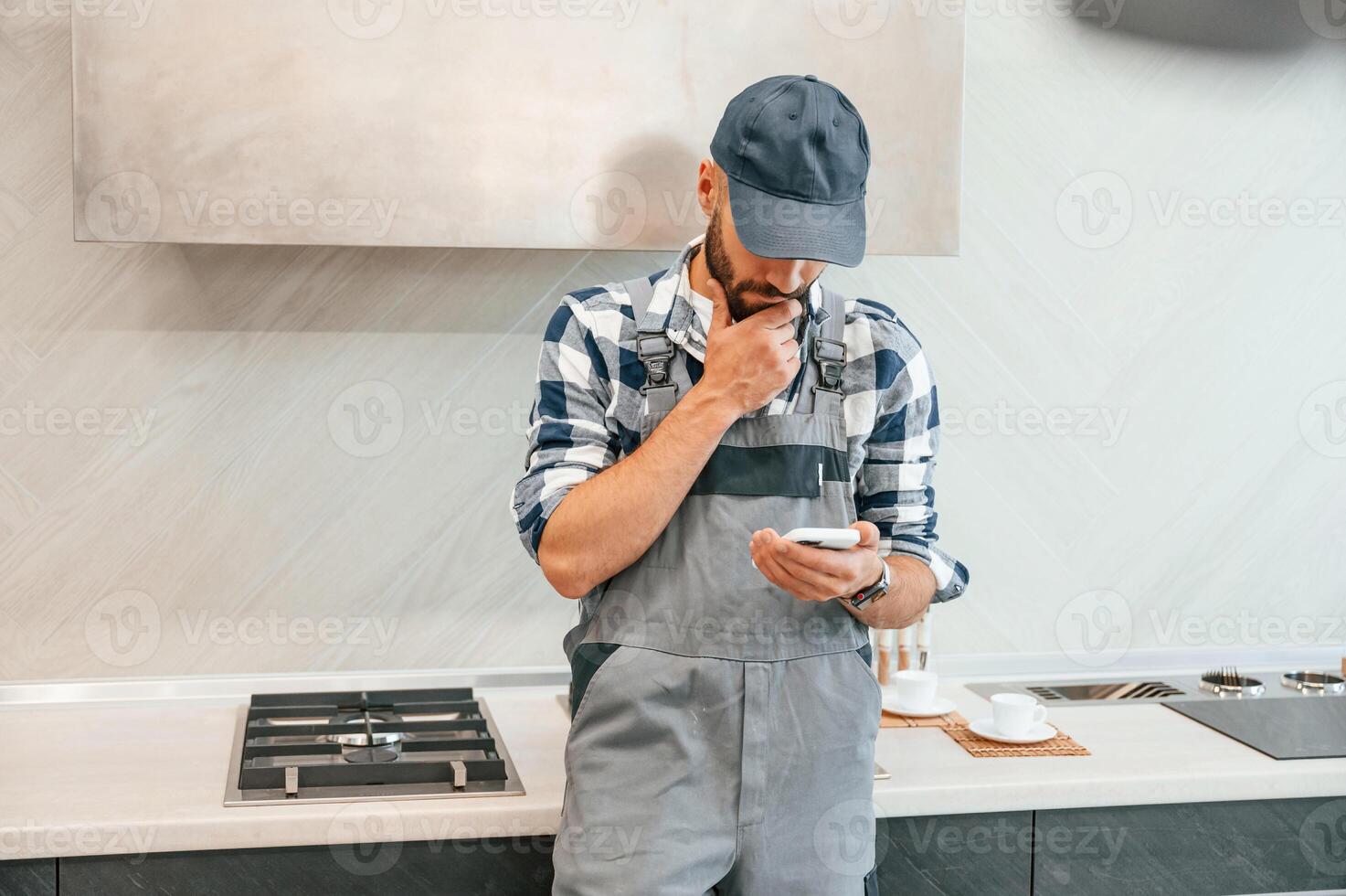 Holding ,smartphone in hand. Plumber in uniform is indoors at home photo