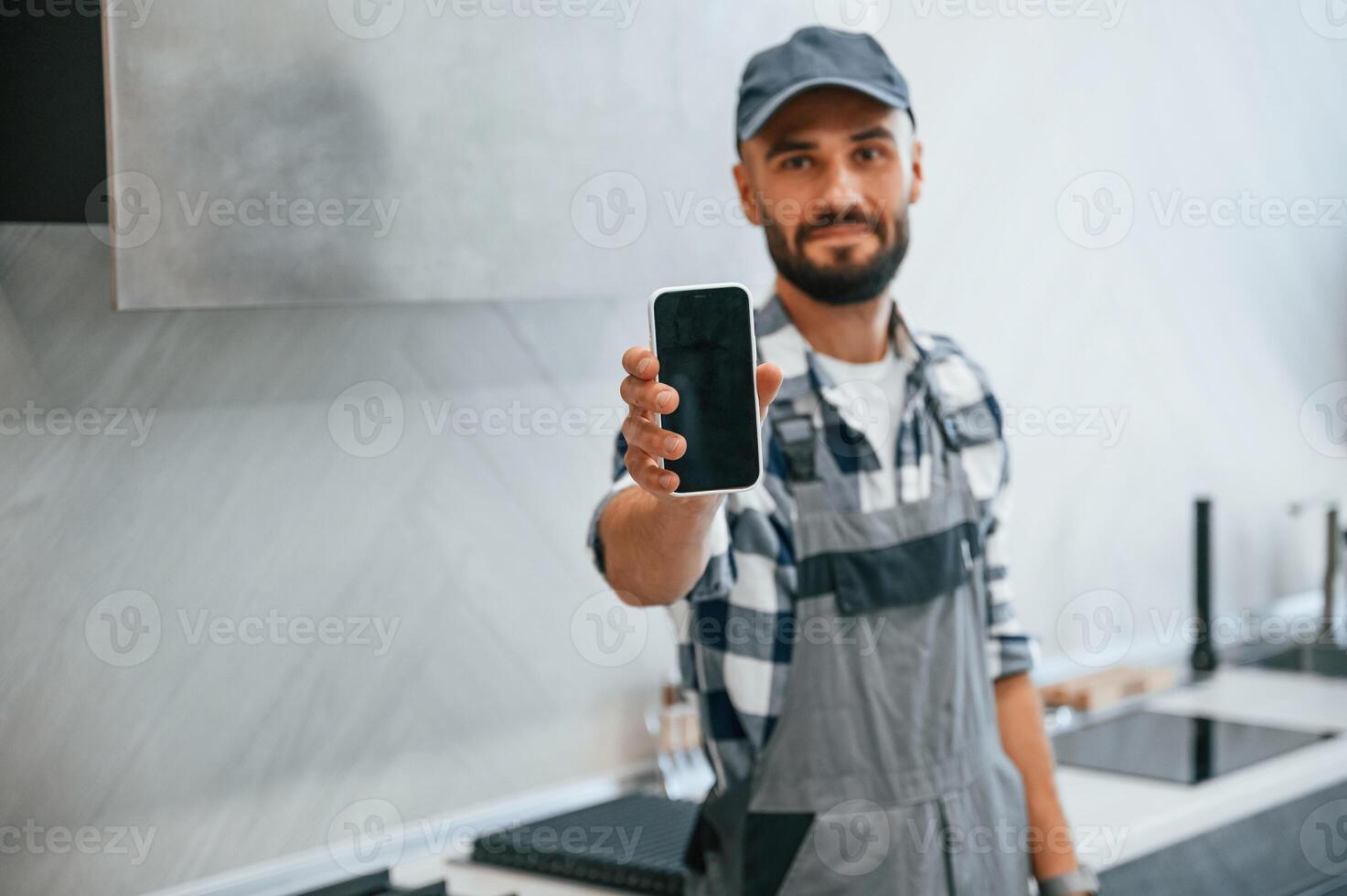 Holding, smartphone, in hand. Plumber in uniform is indoors at home photo