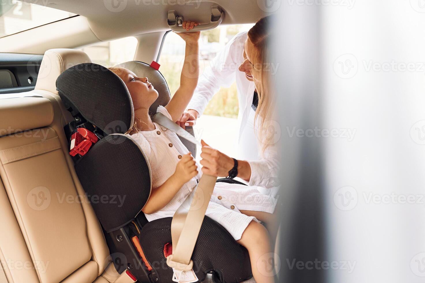 Girl is in a special baby seat. Young woman with her little daughter is with their electric car outdoors photo
