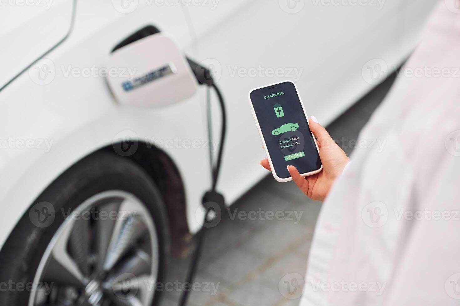 Close, up view. Woman charging her electric car and monitoring process on smartphone photo