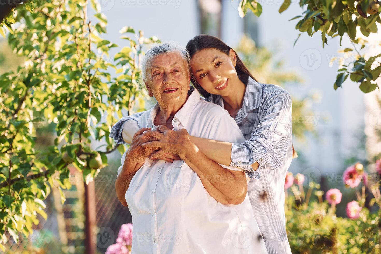 Embracing and posing for a camera. Young woman is with her senior mother is in the garden photo