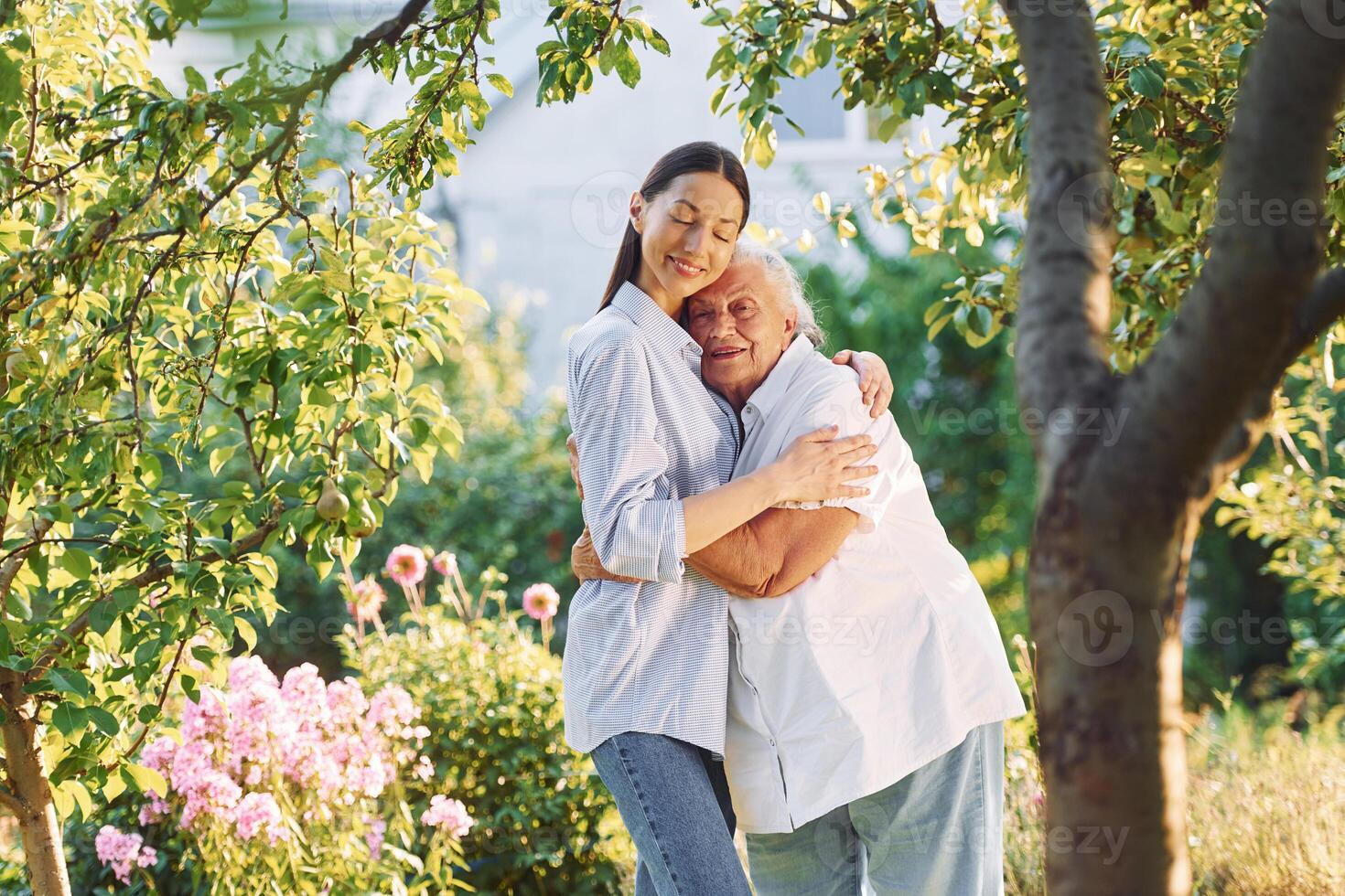 Standing t,ogether and embracing each other.. Young woman is with her senior mother is in the garden photo