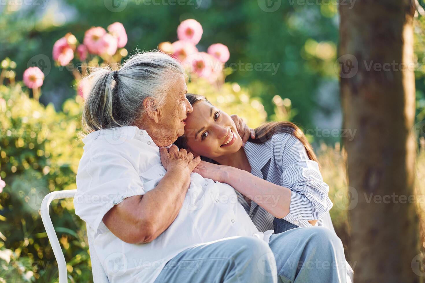 Sitting and embracing each other. Young woman is with her senior mother is in the garden photo
