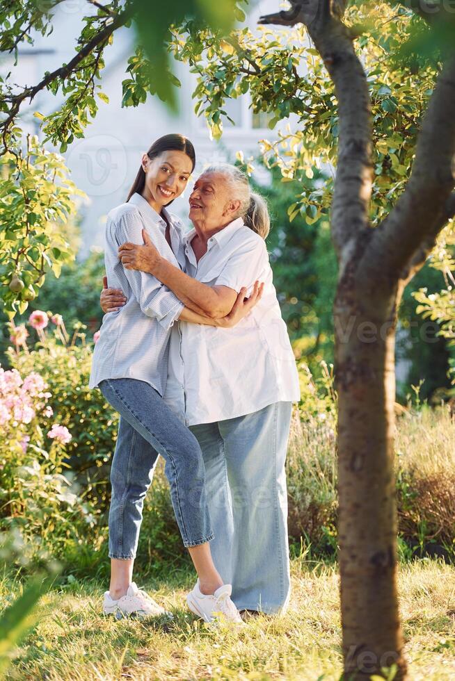 Embracing and, posing for a camera. Young woman is with her senior mother is in the garden photo