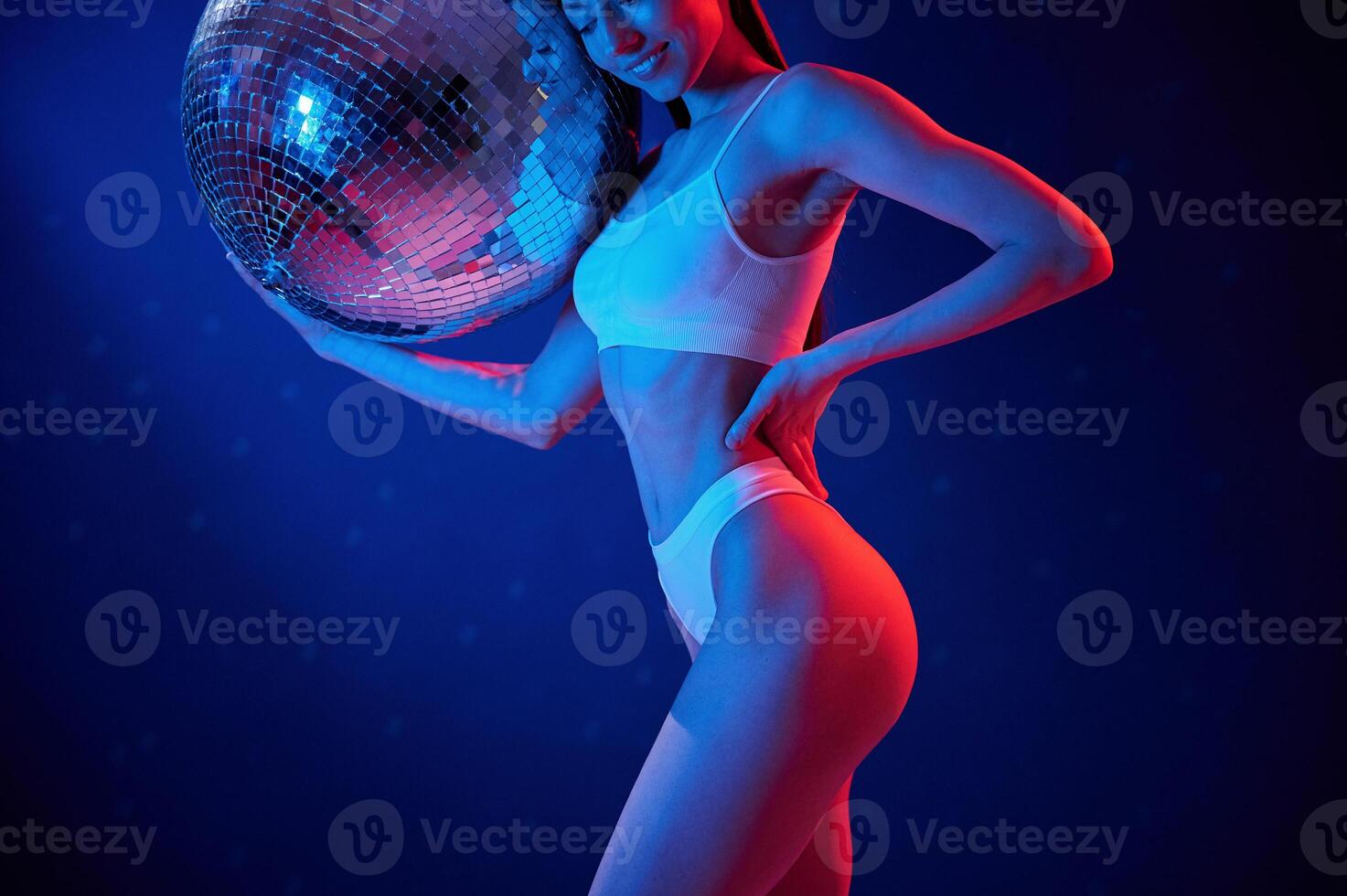 With shiny, mirrored ball. Young woman in underwear is in the studio with neon lights photo
