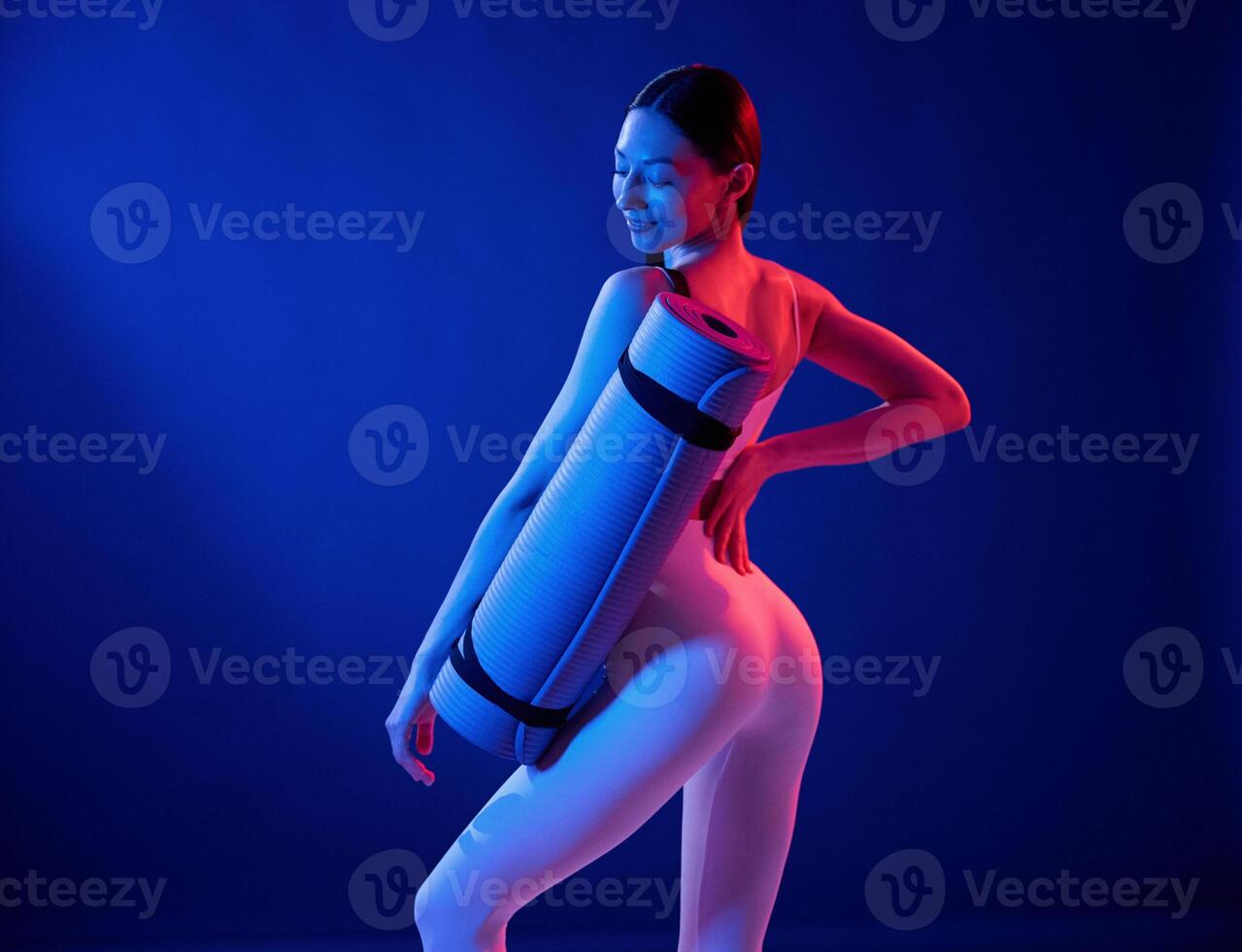 Standing with ,yoga mat. Young woman in sportive clothes is in the studio with neon lights photo