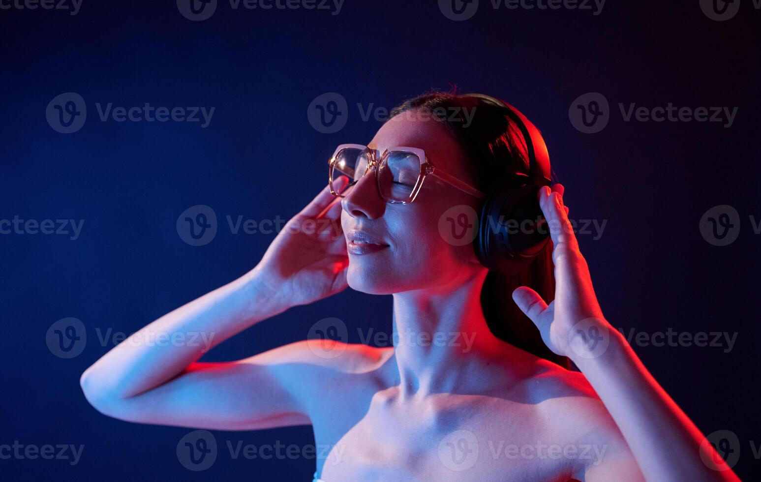 Enjoying ,music by using headphones. Portrait of young woman that is indoors in neon lighting photo