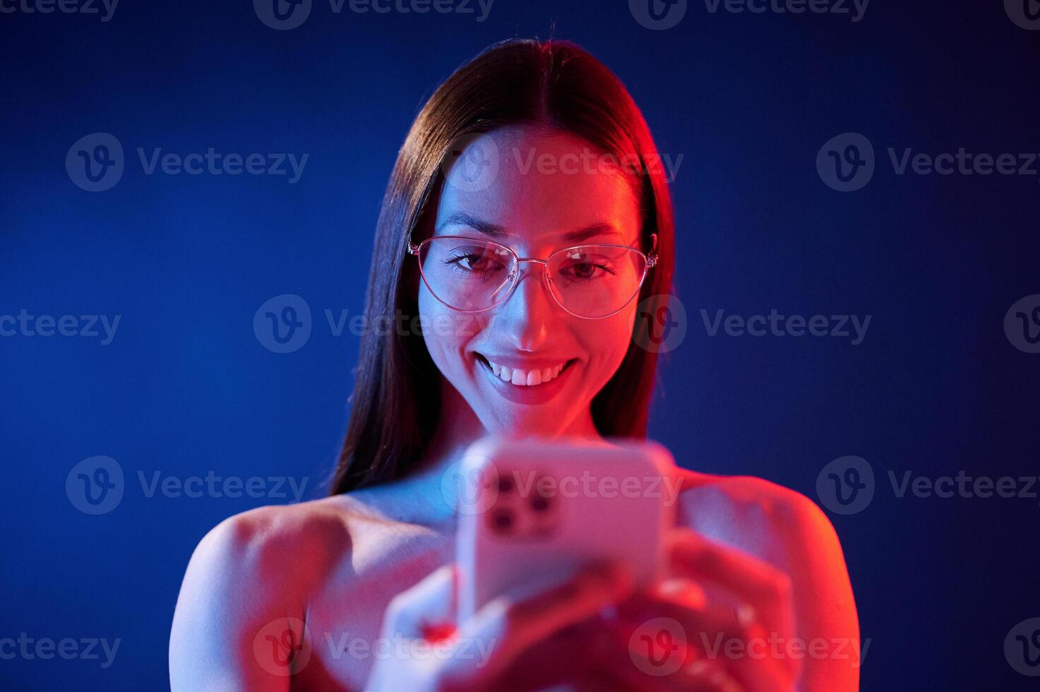 Holding, smartphone and smiling. .Portrait of young woman that is indoors in neon lighting photo
