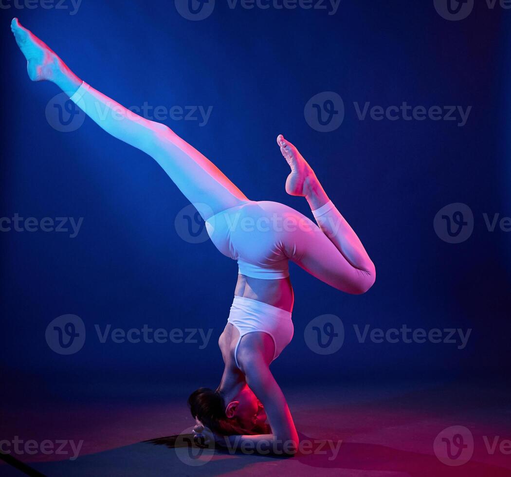 Doing head, stand. Young woman in sportive clothes is in the studio with neon lights photo