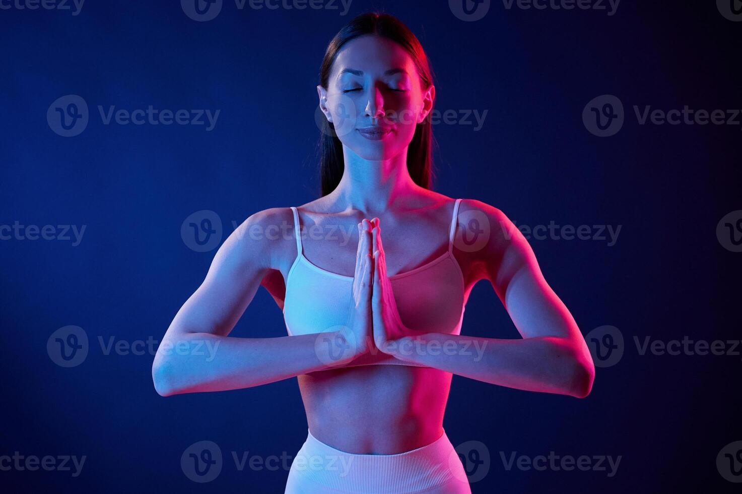 Lotus pose. Young woman in sportive clothes is in the studio with neon lights photo