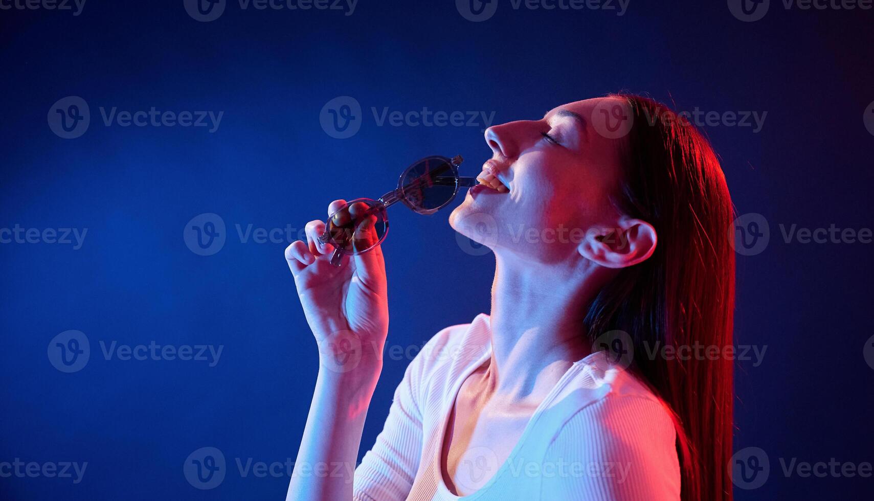 Holding ,sunglasses. Portrait of young woman that is indoors in neon lighting photo