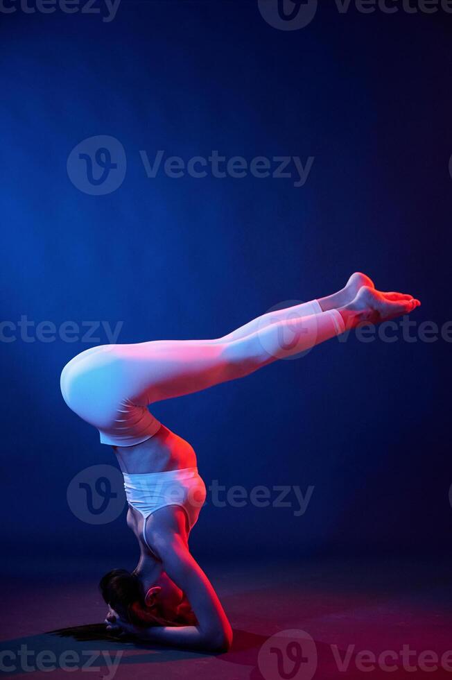 Doing head ,stand. Young woman in sportive clothes is in the studio with neon lights photo
