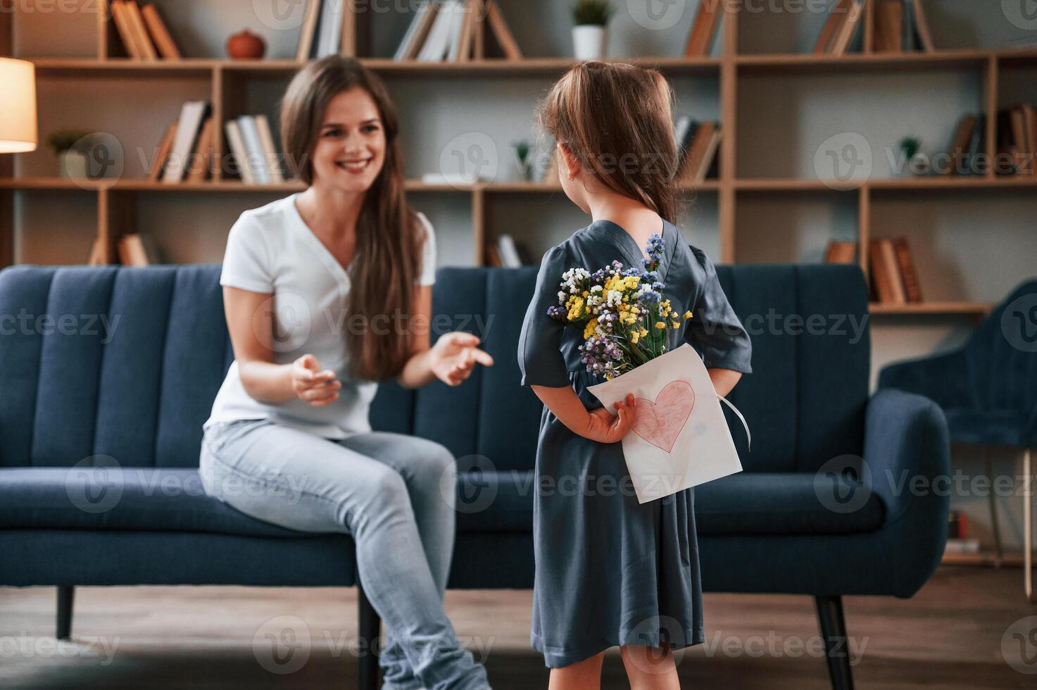 Girl giving ,flowers to mother and holding, love letter. Young woman with her daughter is together at apartment photo