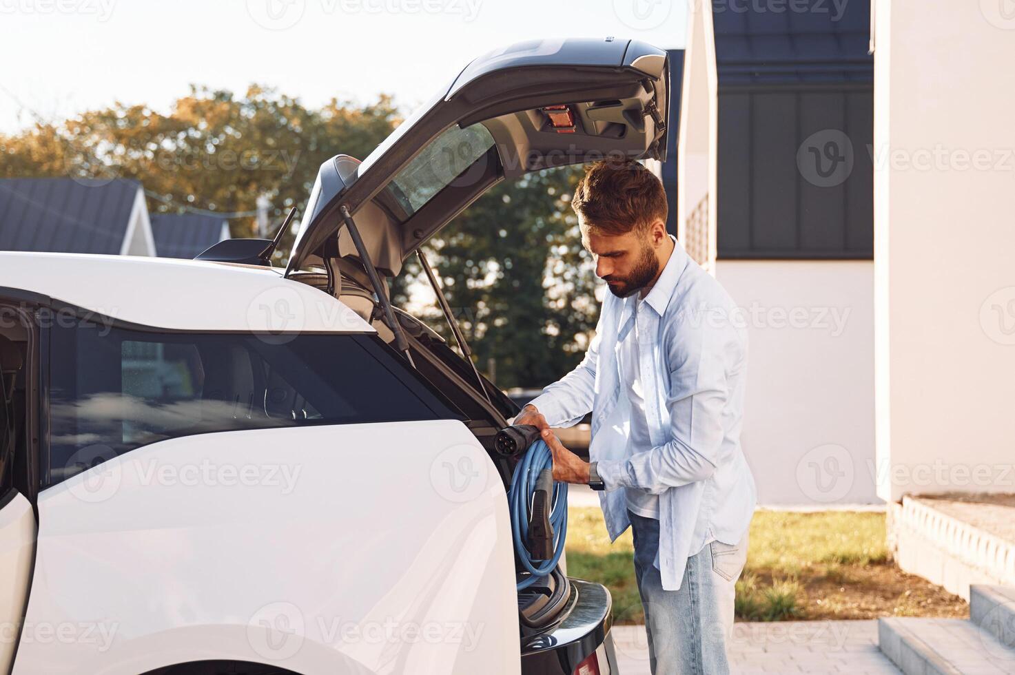 Taking ,charging wire from the truck. Young stylish man is with electric car at daytime photo