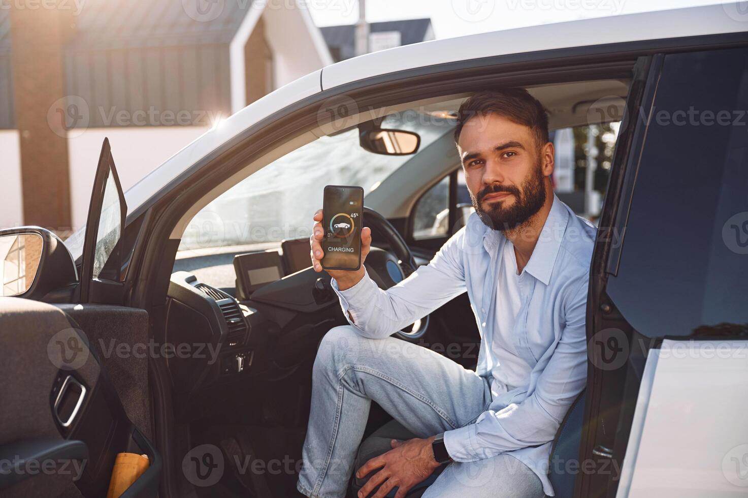 Monitoring ,charging procces by ,using smartphone. Young stylish man is with electric car at daytime photo