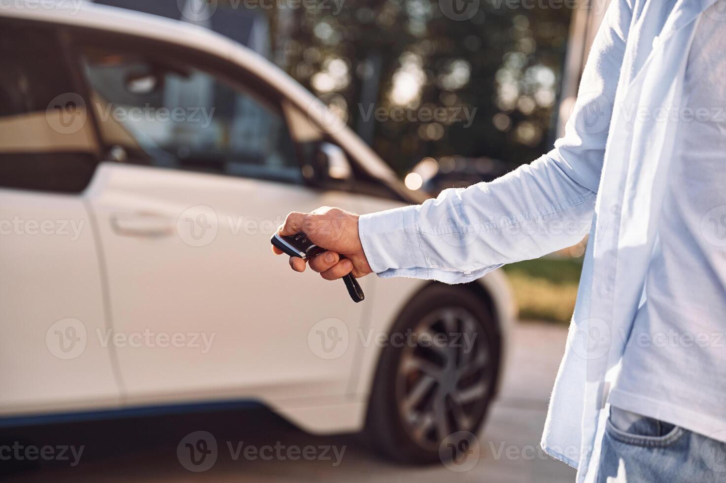 Standing with keys and locking the automobile. Close up view of man with his electric car photo