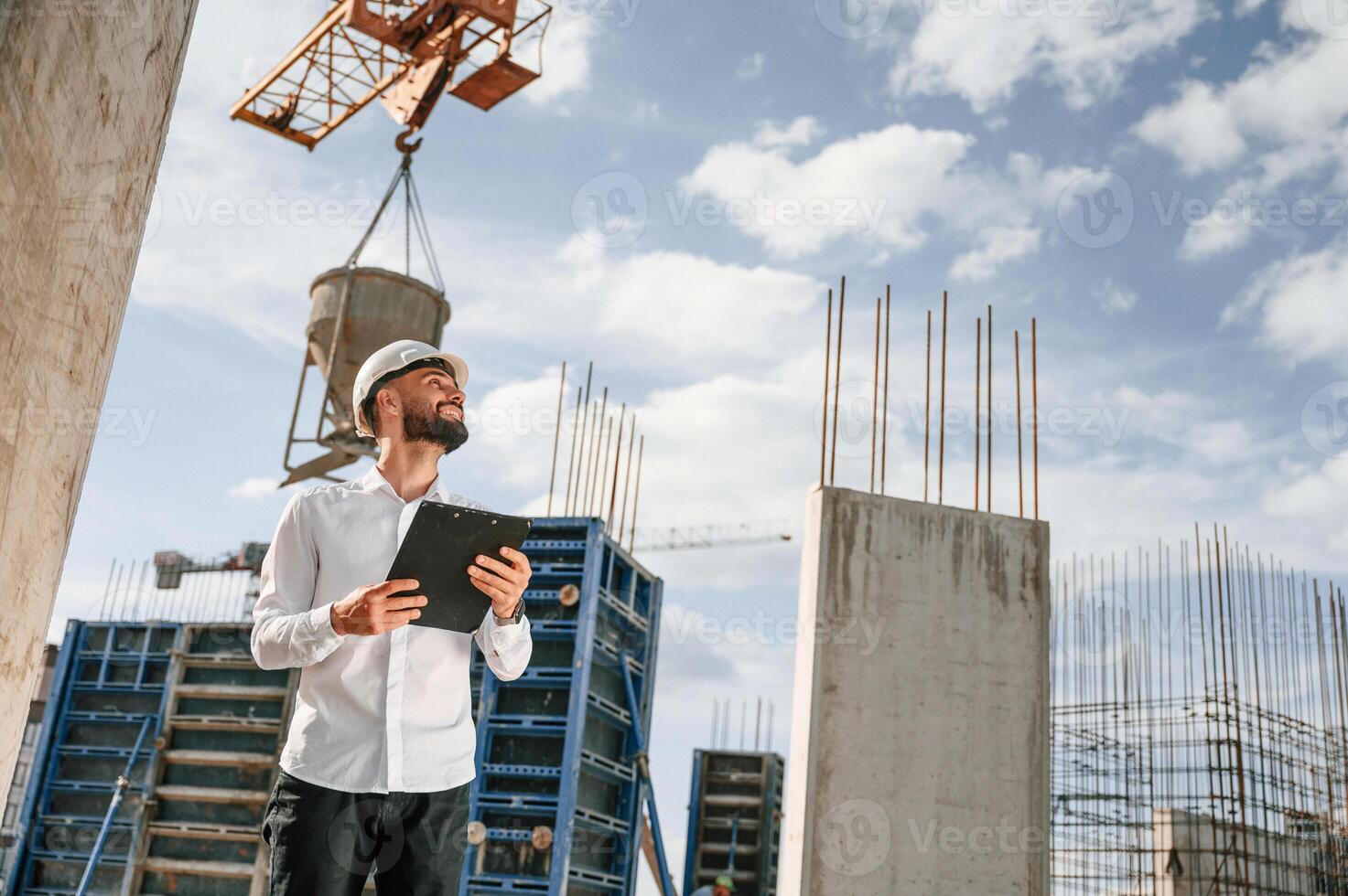 Engineer, is holding notepad. Man in uniform is working on the construction site, photo