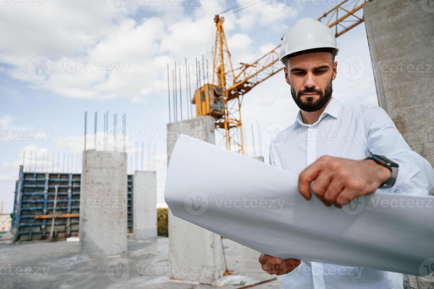 Standing ,and holding plan in hands. Man in uniform is working on the construction site photo