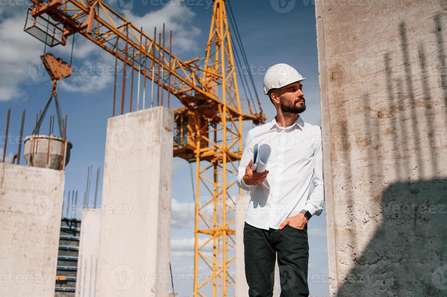 Standing and holding plan in hands. Man ,in uniform is working on the construction site photo