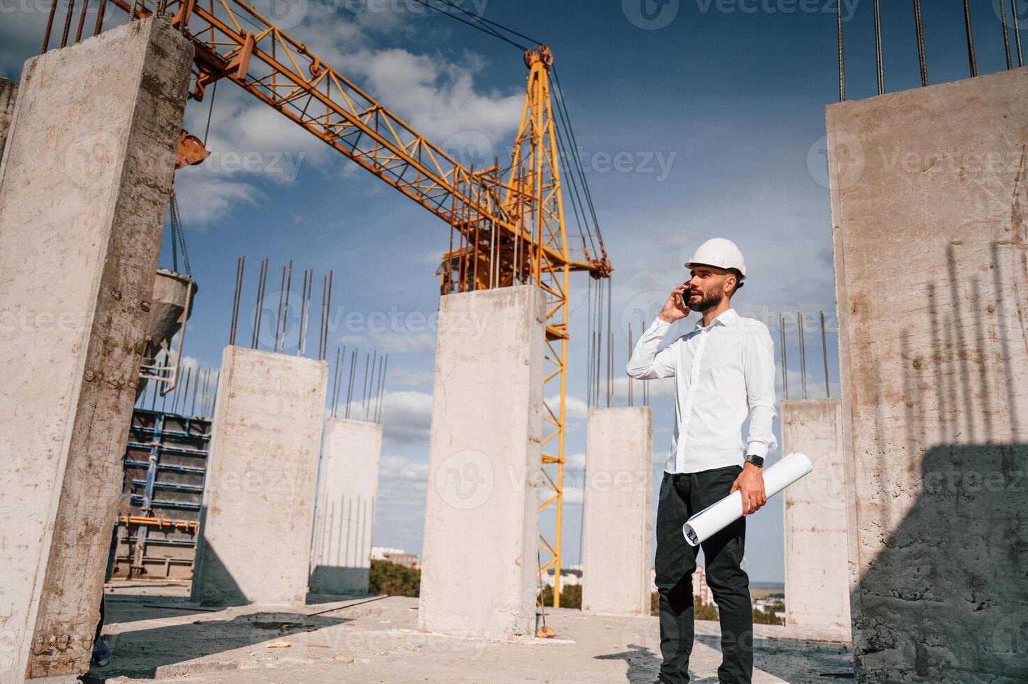 Talking, by phone and holding document in hands. Man in uniform is working on the construction site photo