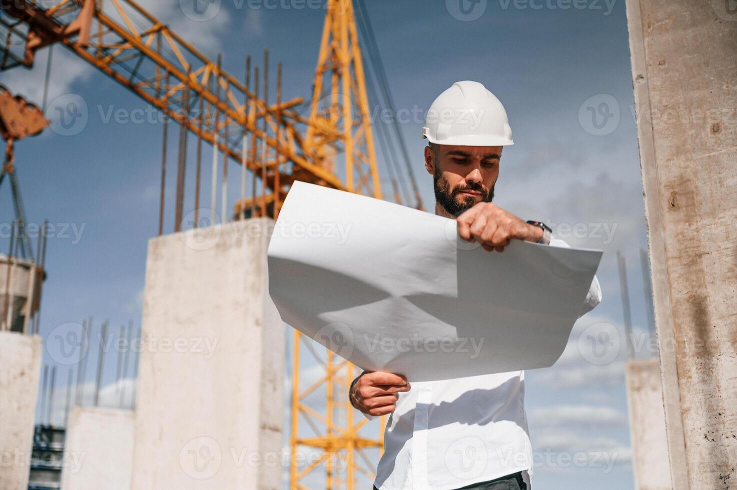 Inspecting a plan. Man in uniform is working on the construction site photo