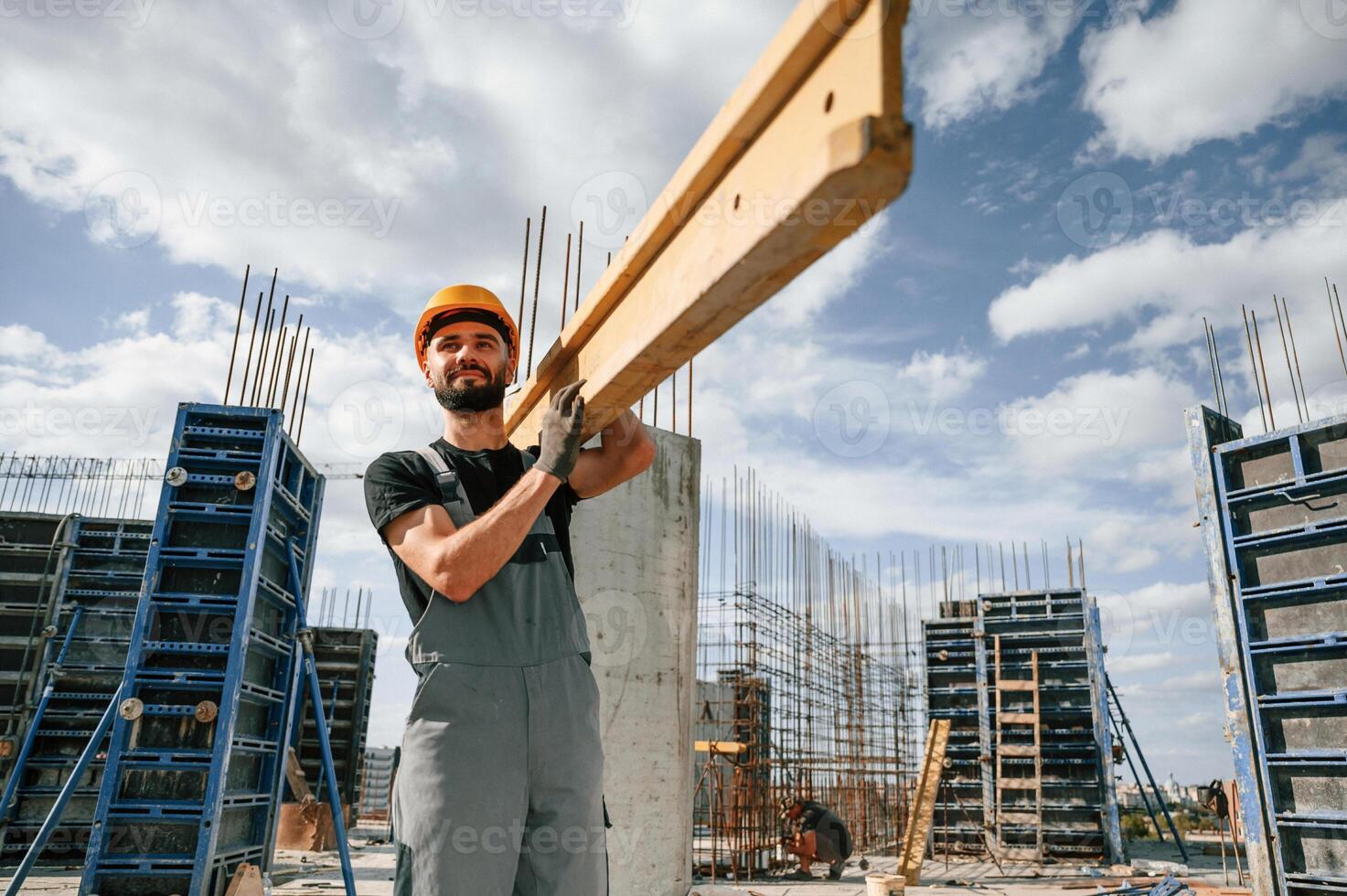 Front view.. Carrying ,wooden plank. Man in uniform is working on the construction site. photo