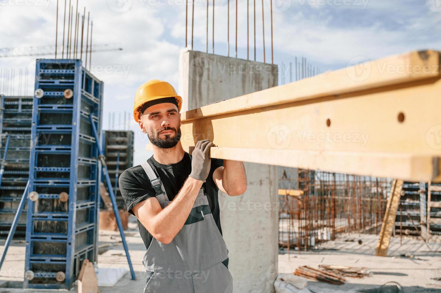 Carrying ,wooden plank. Man in uniform is working on the construction site photo