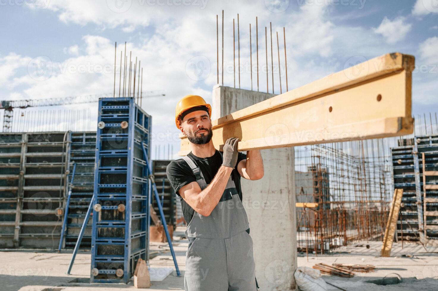 Carrying ,wooden plank. Man in uniform ,is working on the construction site photo