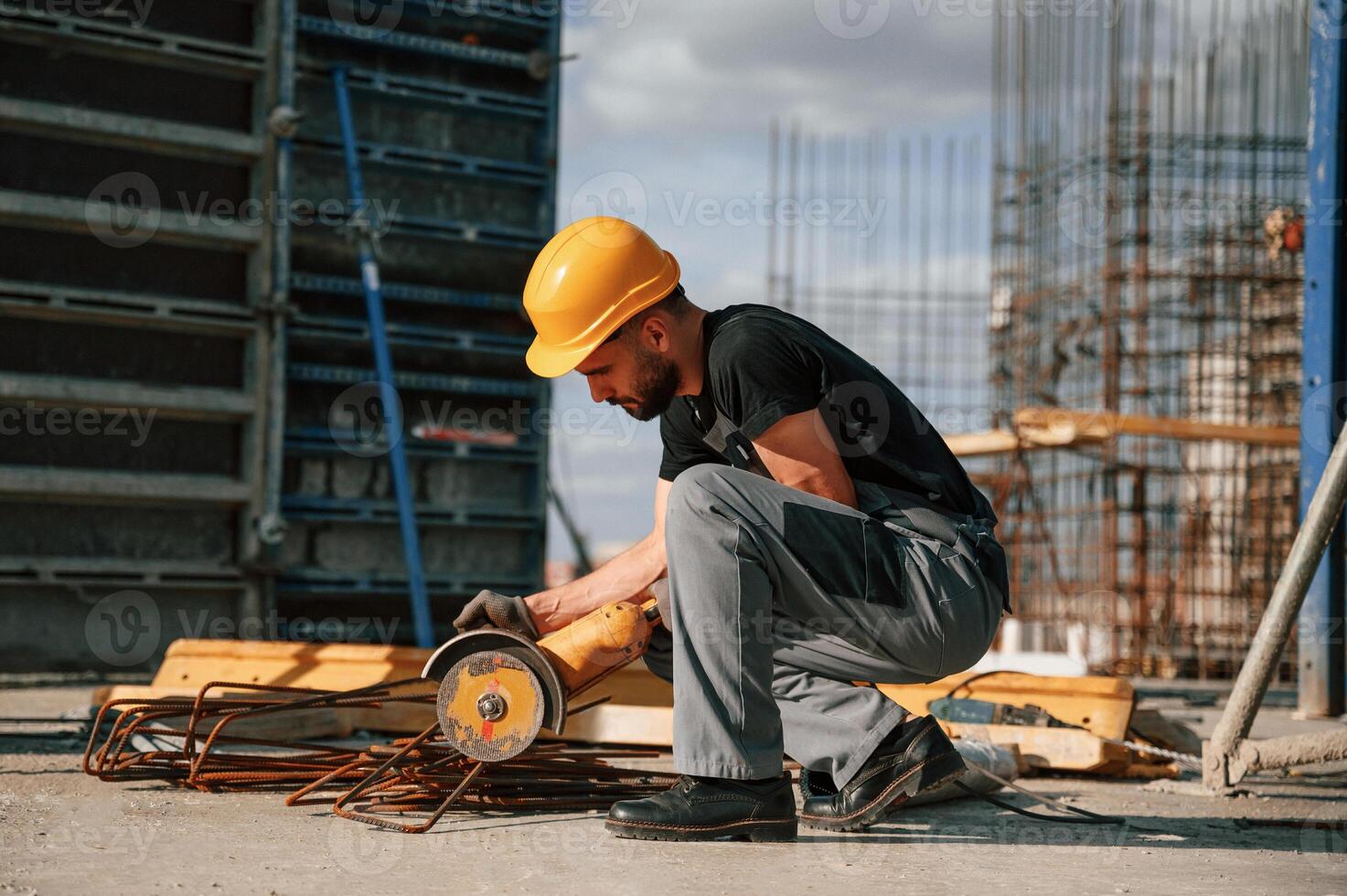 Sitting a,nd cutting metal pieces by grinding machine. Man in uniform is working on the construction site photo