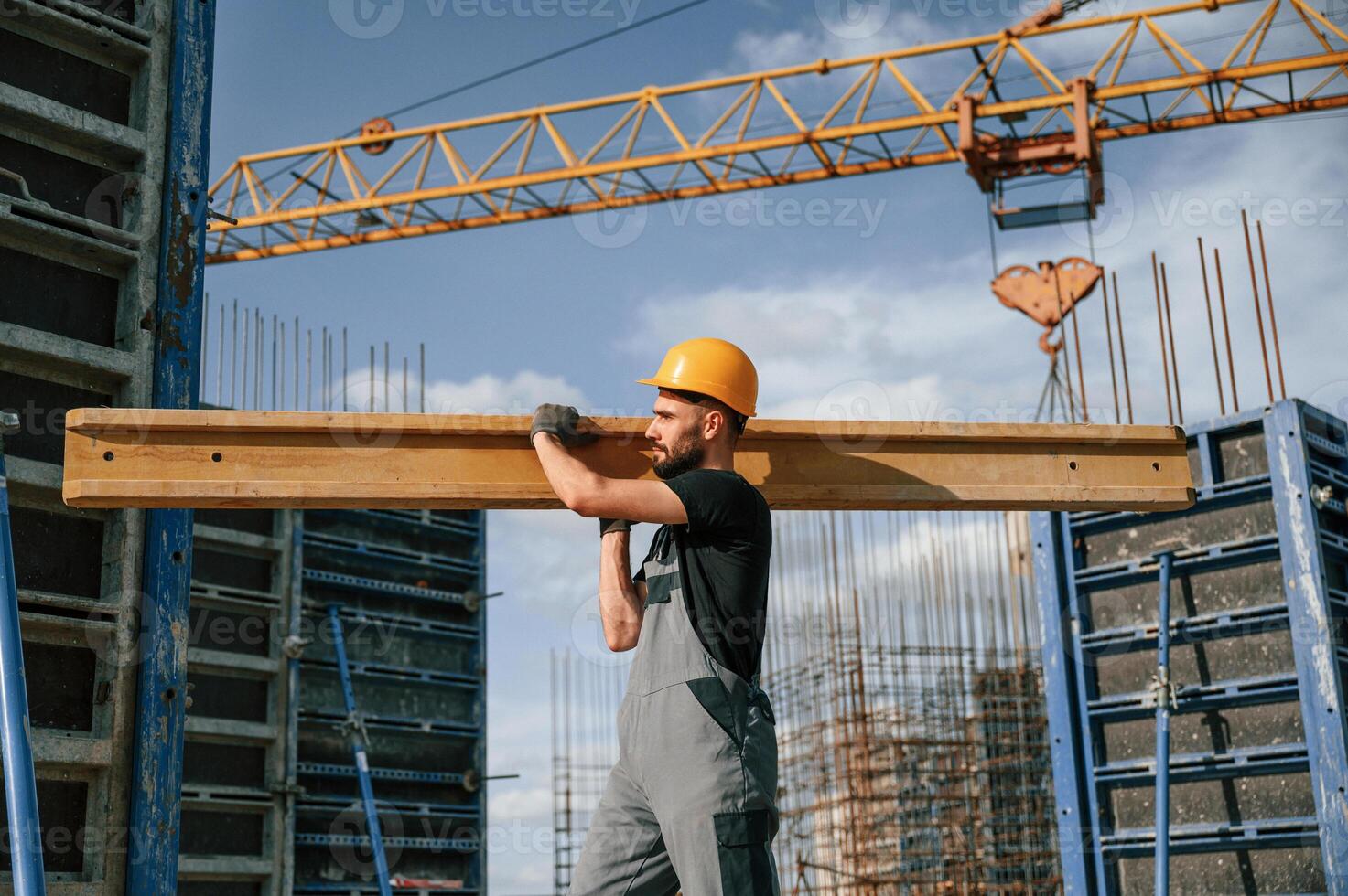 Against crane ,with wooden plank.. Man in uniform is working on the construction site photo