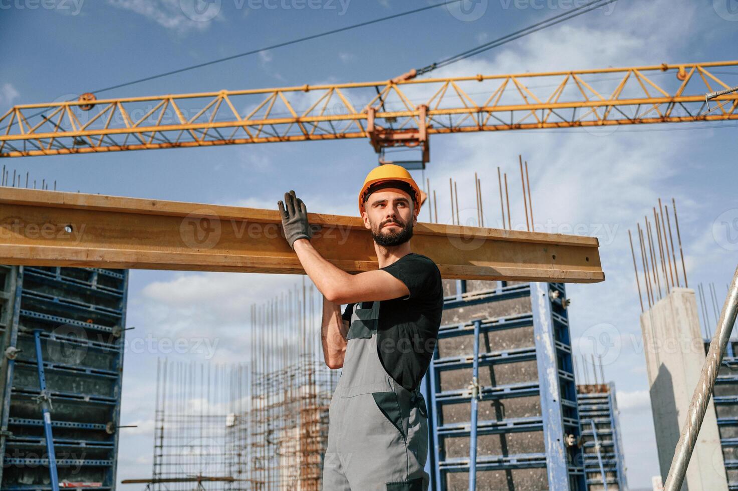 Against crane with wooden plank. Man in uniform is working on the construction site photo