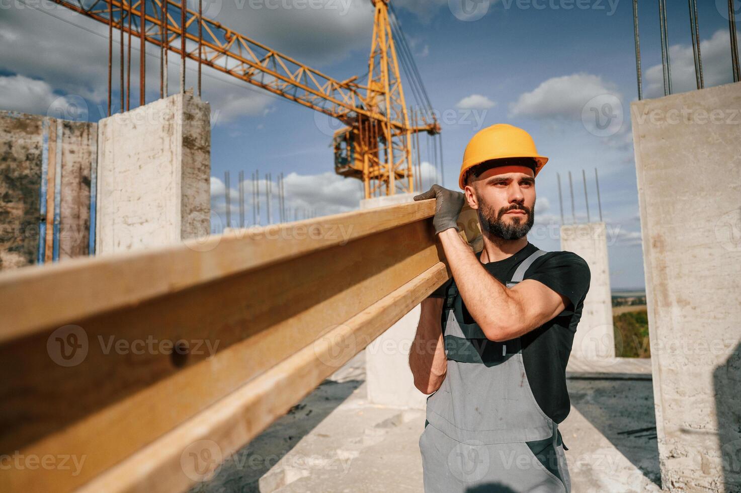 Front view of man, that is in uniform holding wooden plank on the construction site photo