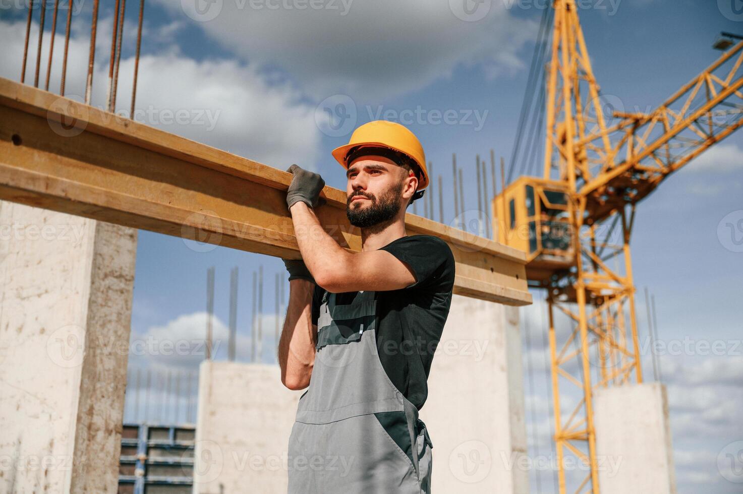 Holding, and walking with wooden plank. Man in uniform is working on the construction site photo