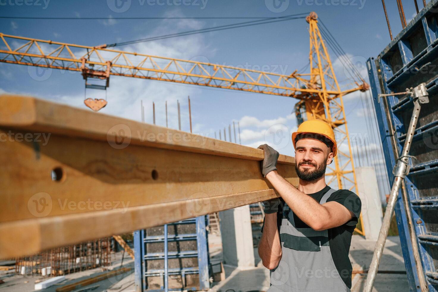 Against crane ,with wooden plank. ,Man in uniform is working on the construction site photo