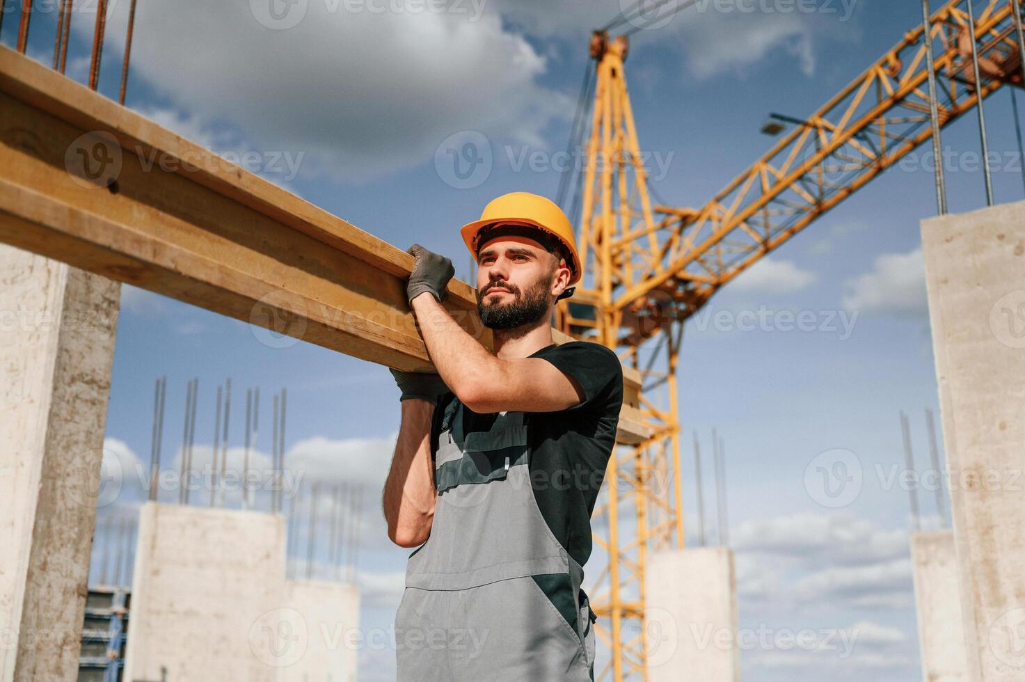 Front view of man that is in uniform holding wooden plank on the construction site photo