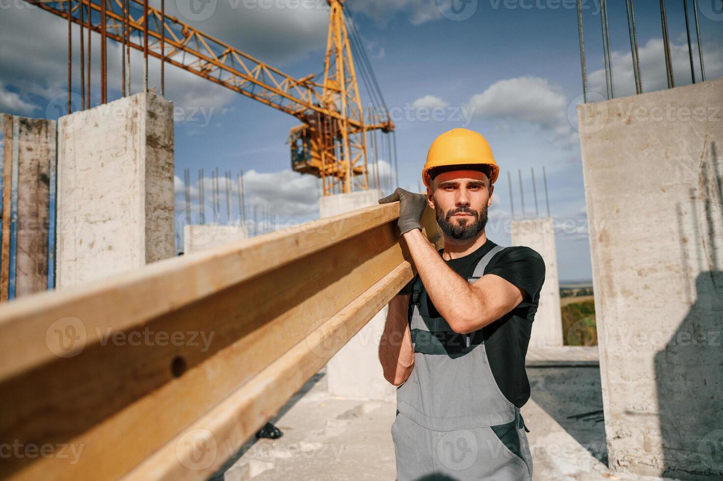 Wooden plank in hands. Man in uniform is working on the construction site photo