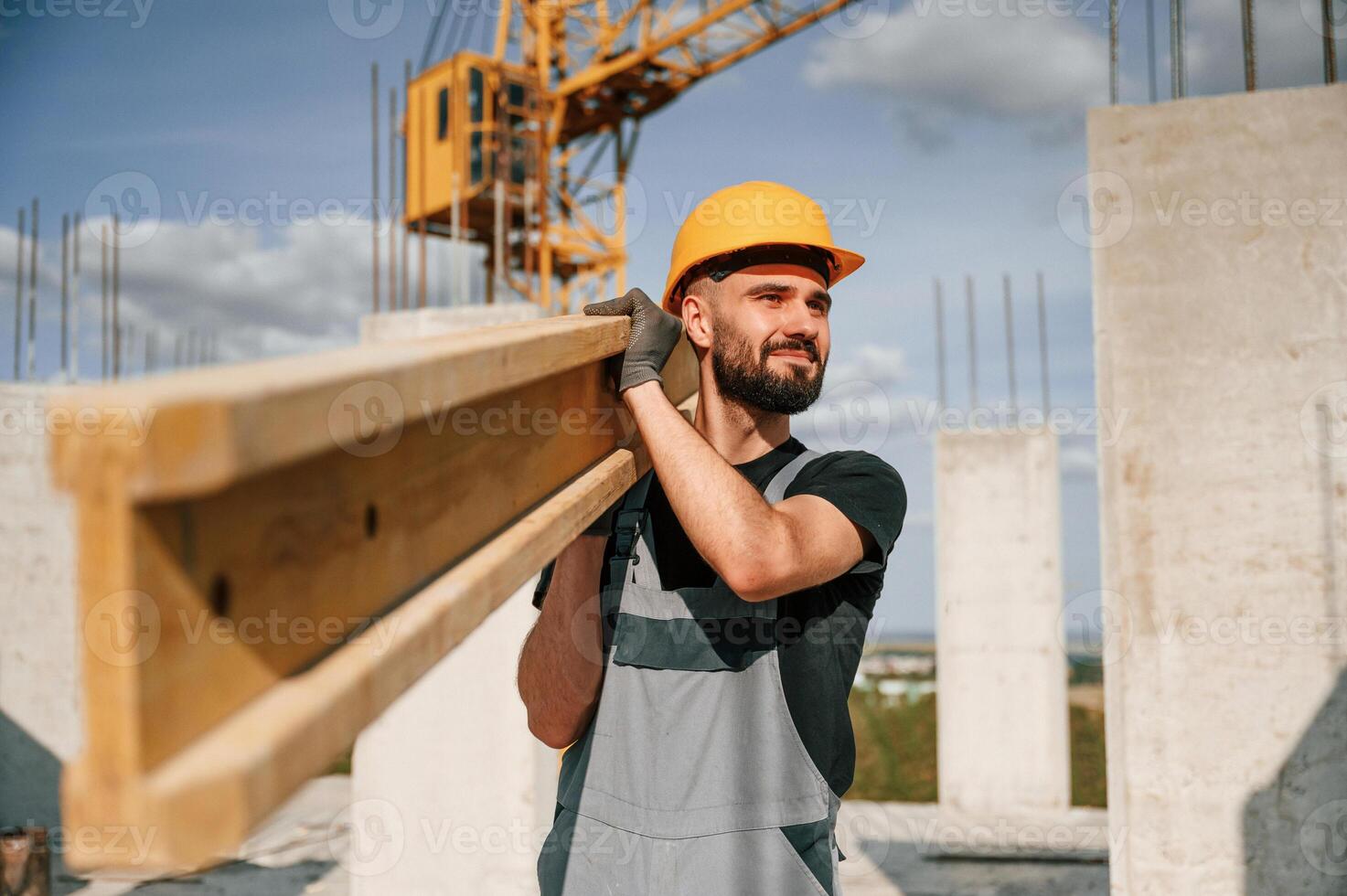 Holding and walking with wooden plank. Man in uniform is working on the construction site. photo