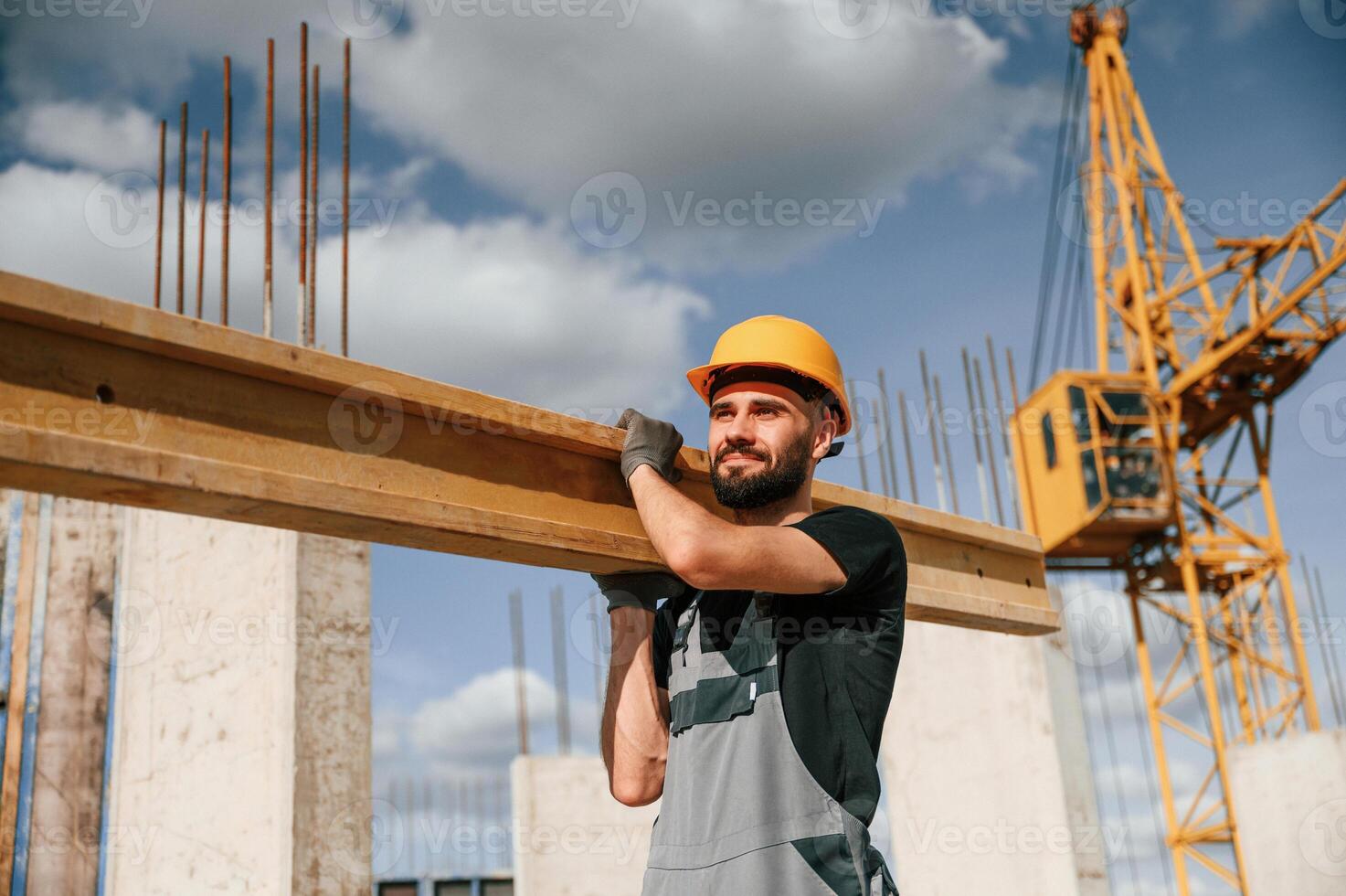 Holding and walking ,with wooden plank. Man in uniform is working on the construction site photo