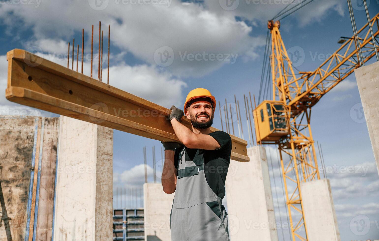 Holding, and walking with wooden plank.. Man in uniform is working on the construction site photo
