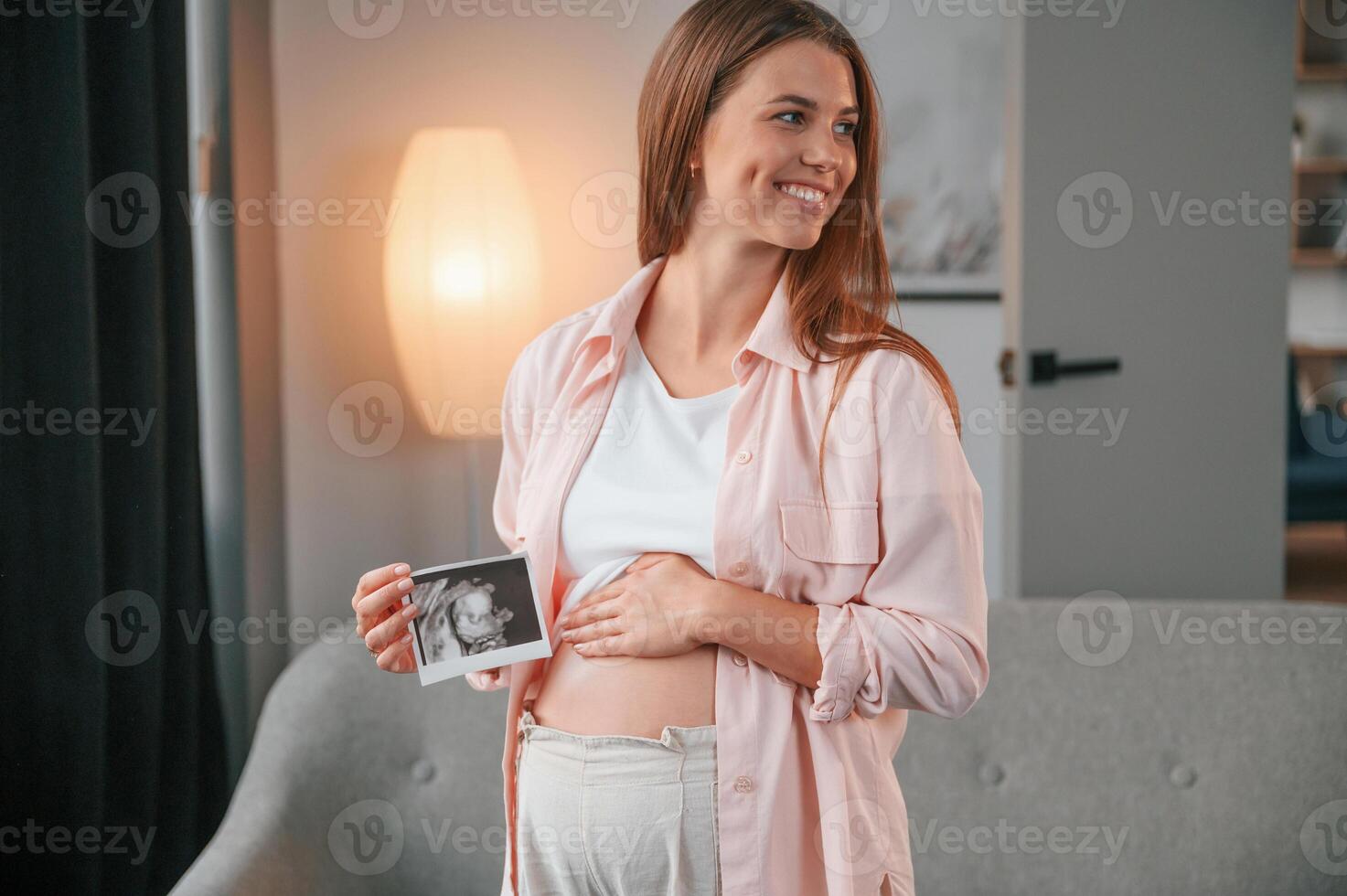 Holding ,ultrasound diagnostics picture of the baby. Beautiful pregnant woman is indoors at home photo
