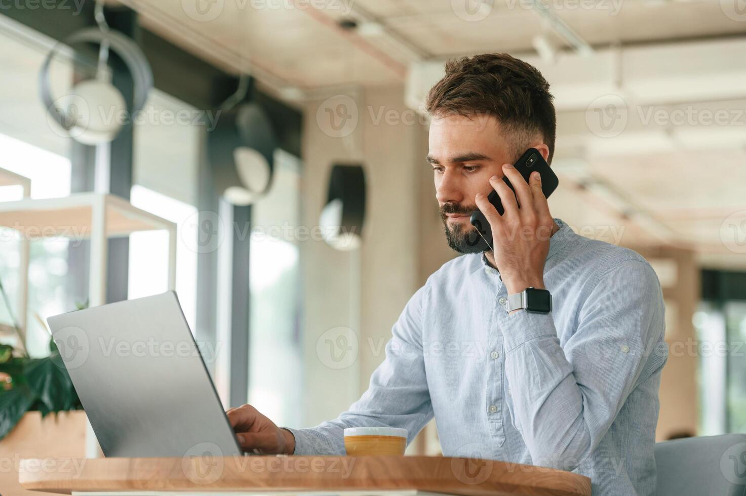 Talking by the phone. Young, man is sitting in the cafe and working by using laptop photo