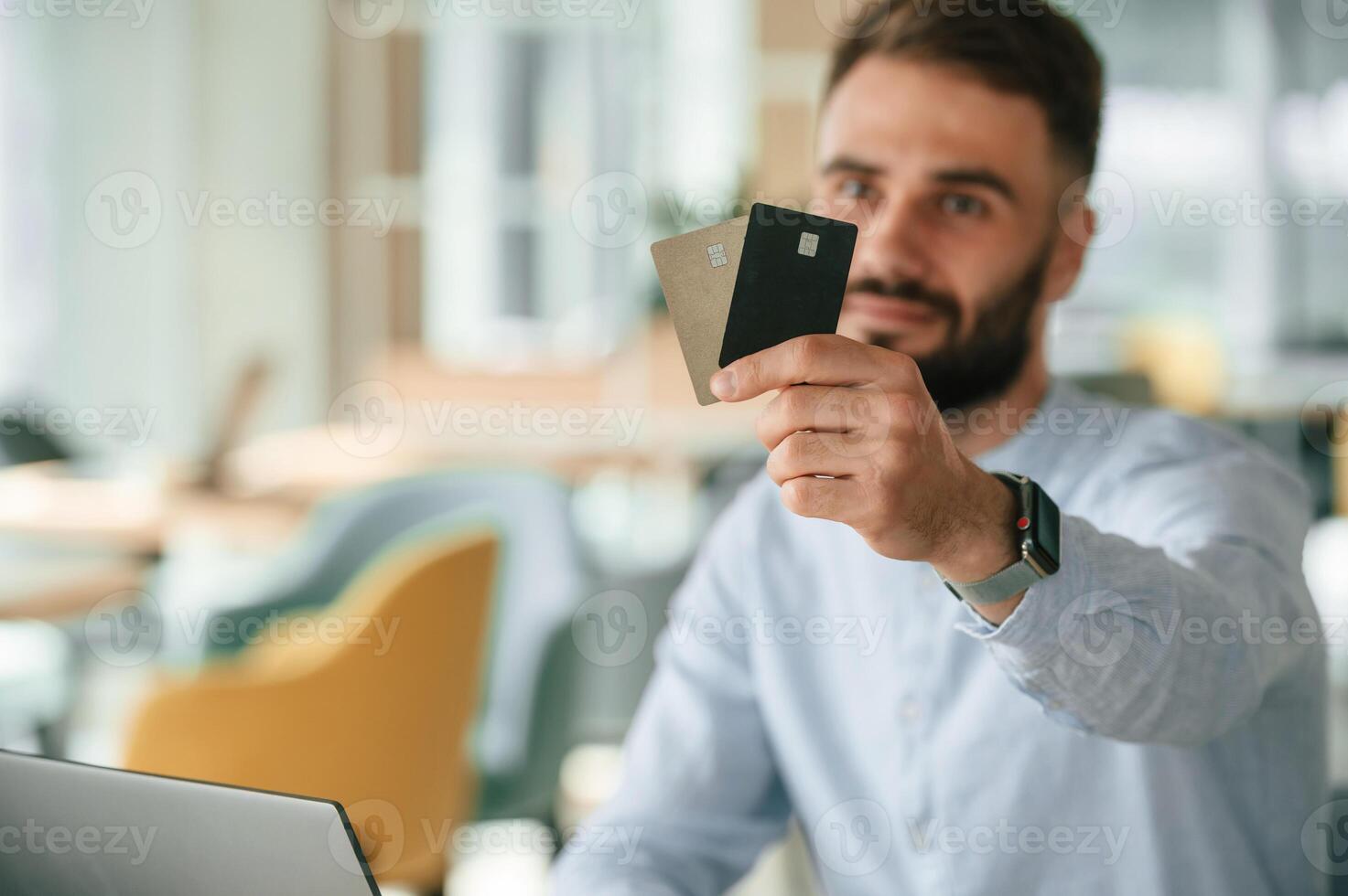 Showing credit cards. Young man is sitting in the cafe and working by using laptop photo