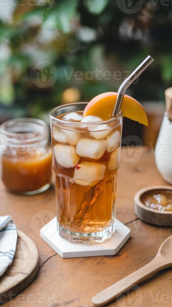 A glass of iced tea with a spoon and a peach on a wooden table photo