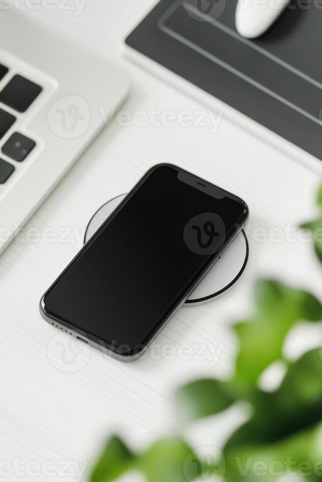 A smartphone is placed on a desk next to a laptop and a mouse photo