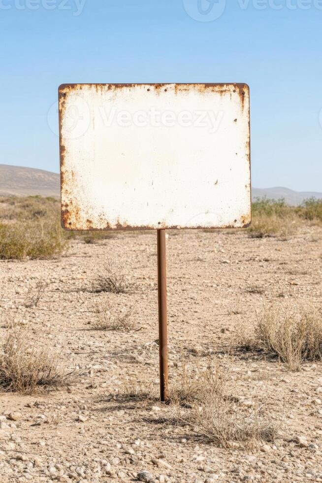 Rusty metal signboard stands alone in a desolate landscape under clear blue skies photo