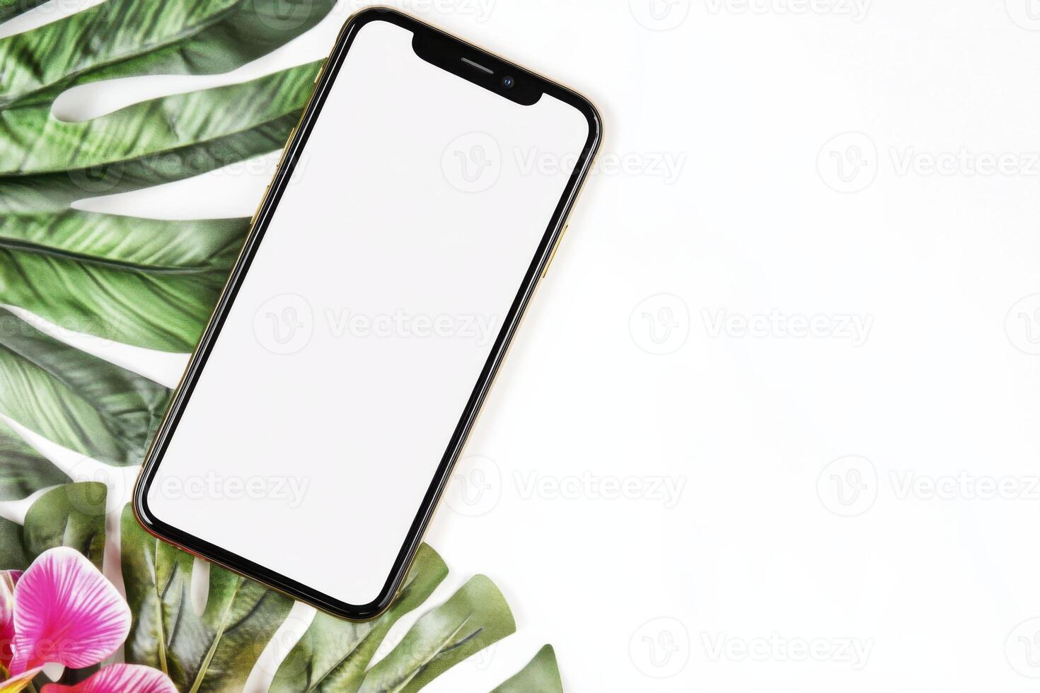 Smartphone with white screen placed on palm leaves against a clean white backdrop photo