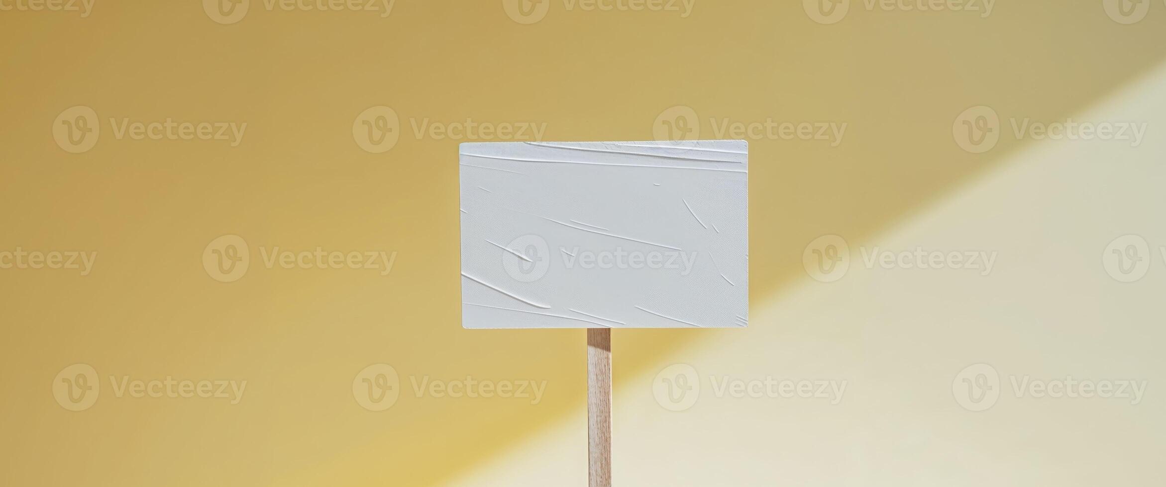 A white square on a stick in front of a yellow wall photo